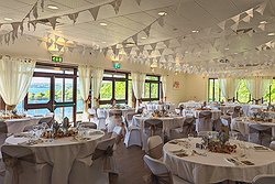 A room of round tables set up for a wedding, with white bunting across the ceiling.